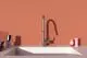Küchenarmatur von Ideal Standard mit einem schlanken, silbernen Auslauf und einem modernen Design, montiert über einem weißen Spülbecken vor einer orangenen Wand.